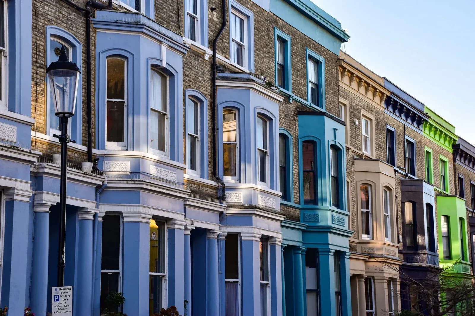 A row of colourful painted terraced houses in Notting Hill, London, with a street lamp under a blue sky.